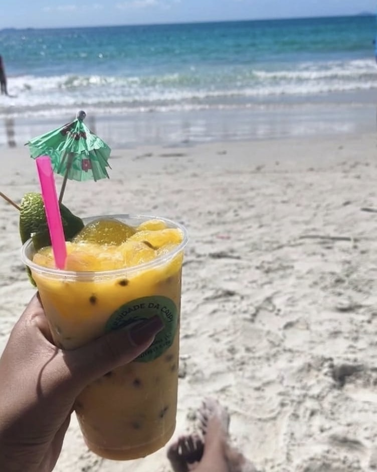 Caipirinha de maracujá na mão com a praia ao fundo