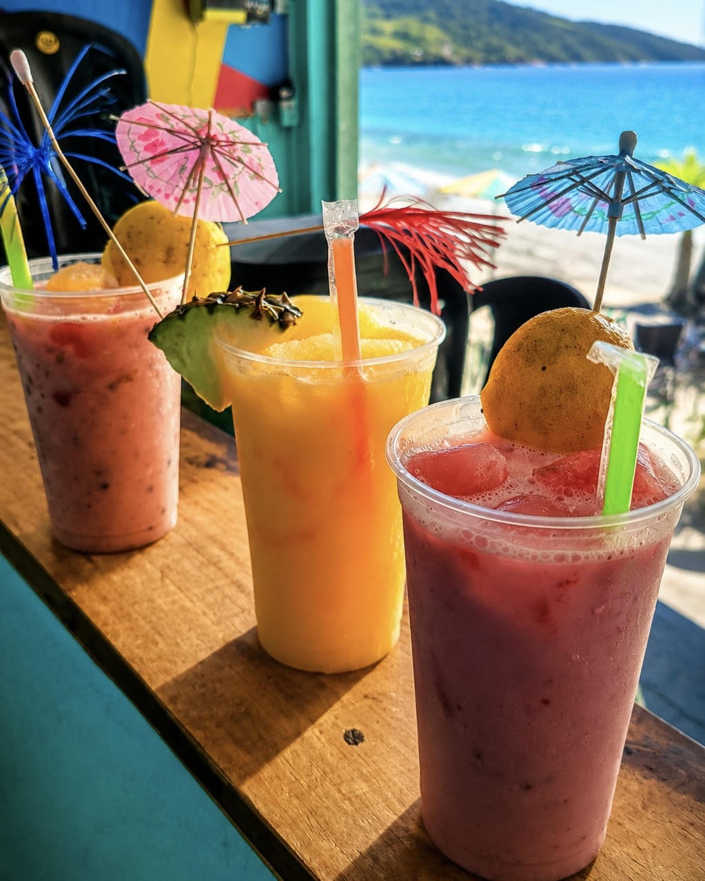 Três caipirinhas de frutas no balcão com vista para o mar
